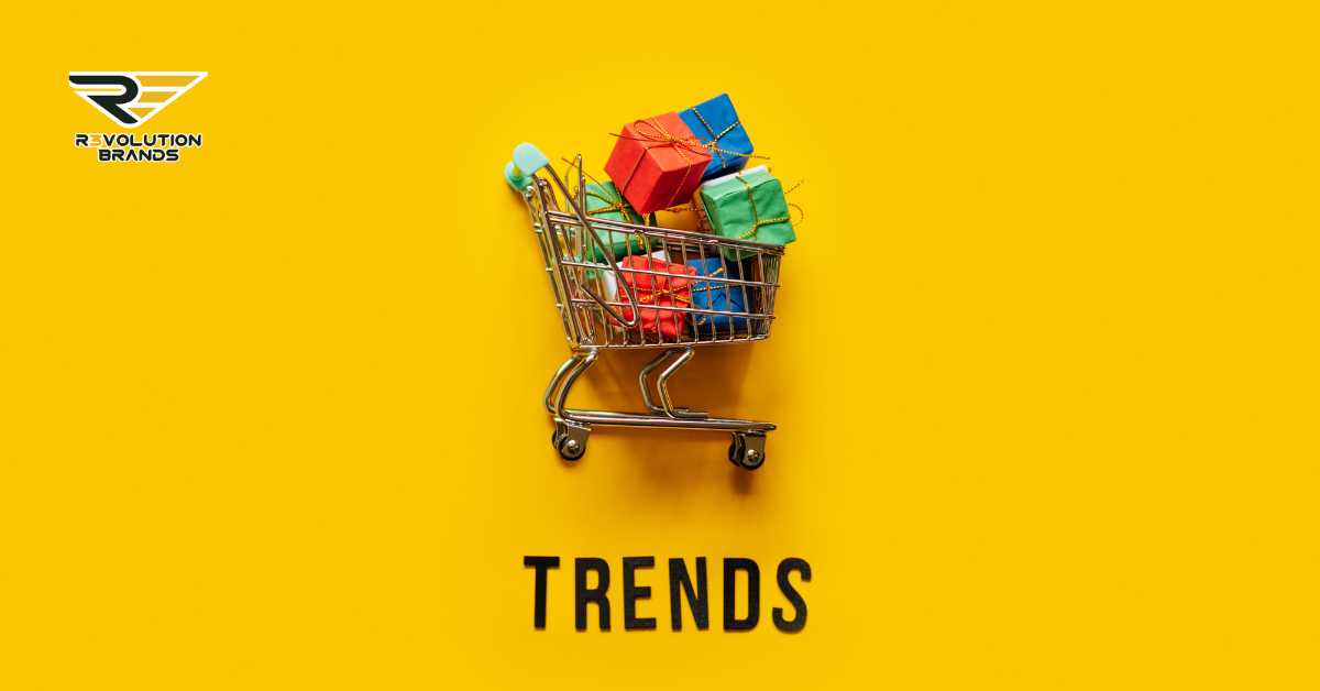 The image creatively visualizes the concept of "shopping for trends," with a shopping cart filled with colorful gift boxes on a bright yellow background, under the word "TRENDS." This represents the idea of selecting or adopting new market trends, much like picking out products from a store. It's an engaging and straightforward metaphor for businesses, like those under Revolution Brands, to keep up-to-date and strategically choose which new movements or consumer behaviors to incorporate into their operations to stay competitive and relevant.