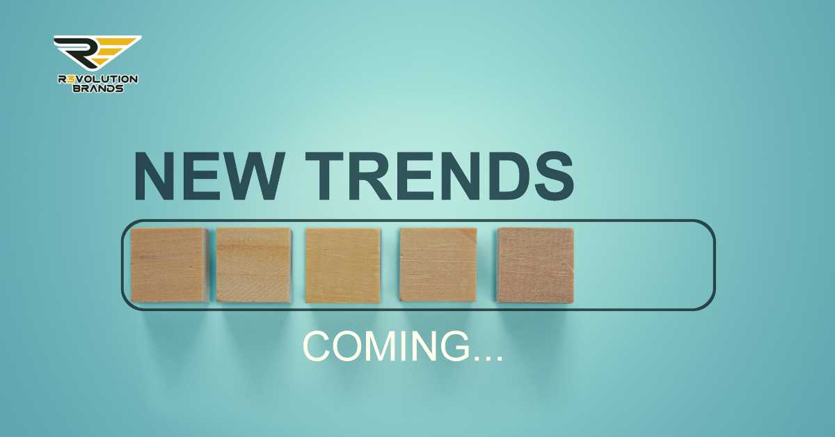 An engaging graphic of a simple yet compelling design with the text 'NEW TRENDS COMING...' displayed on a turquoise background. Four wooden blocks are aligned within a transparent rectangular frame, suggesting the sequential unveiling of future trends. The R3volution Brands logo in the upper left corner accentuates the theme of anticipation and readiness for new developments in the franchise industry.