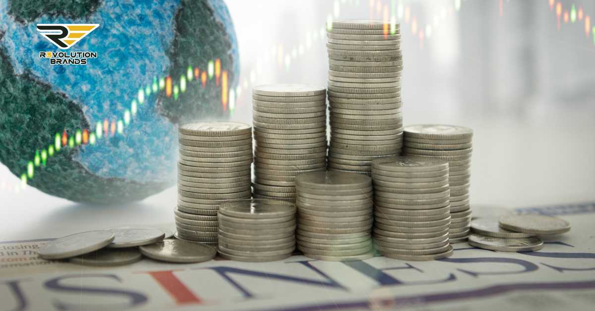 The image depicts several stacks of silver coins of varying heights arranged on top of a newspaper with the headline "BUSINESS". In the background, there is a blurred image of a globe with stock market graphs, suggesting a global financial context. The R3volution Brands logo is visible at the top left, linking the image to the brand and its interest in franchise financing and economic trends. The overall composition conveys themes of finance, investment, and the dynamics of the global market, relevant to discussions on economic growth and financial strategies in franchising.