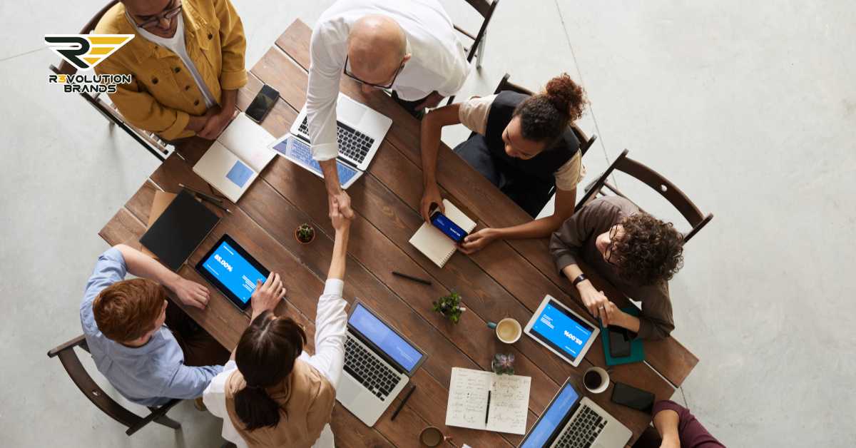 Top view of a diverse team of R3volution Brands professionals engaged in a strategic meeting, using laptops and digital devices to discuss leadership and franchise strategies for 2024.