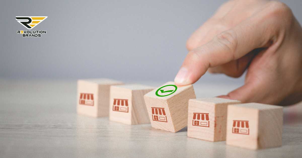 A hand placing the final wooden block with a green checkmark on top, completing a line of blocks each stamped with a store icon. This image symbolizes the successful selection or approval in the franchising process, with each block representing a step towards achieving a franchise goal. The R3volution Brands logo in the upper left corner reinforces the brand's focus on guiding new franchisees through the franchising landscape.