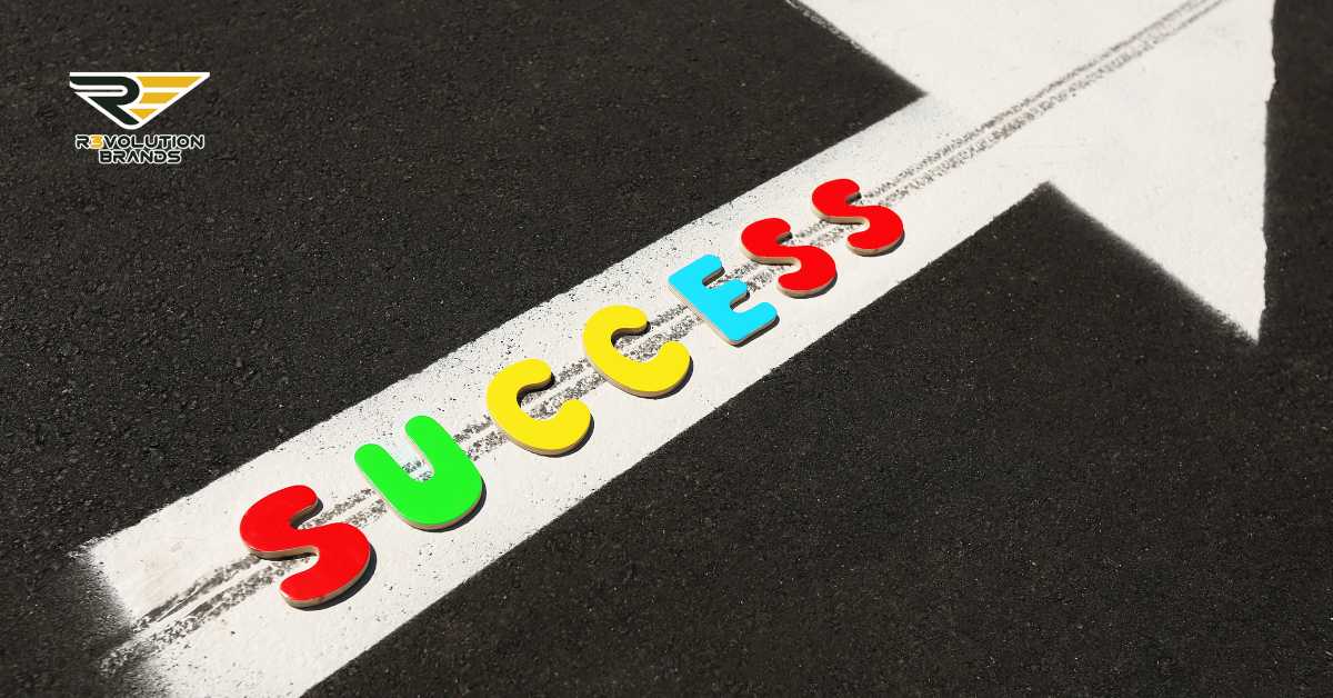 This image vividly represents the theme of business success, illustrated by the word "SUCCESS" in colorful letters laid out across a finishing line on a racetrack. The imagery suggests the idea of crossing into successful outcomes, with a focus on achieving goals. The asphalt background and the stark white line enhance the visual metaphor of the business journey. This could symbolize the culmination of strategic planning and effort in reaching business objectives, particularly within the context of franchise growth or entrepreneurial endeavors as emphasized by the Revolution Brands logo.