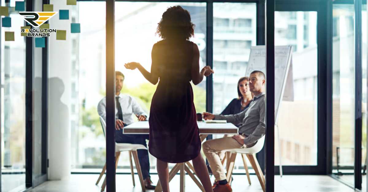 Businesswoman leading a meeting at R3volution Brands, discussing innovative management practices in a bright, modern office setting with a team of engaged professionals.