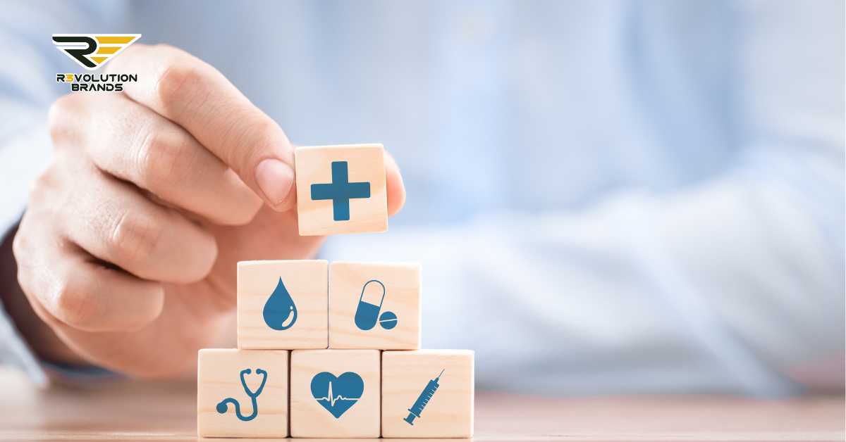 The image features a hand positioning a wooden block with a blue plus symbol on it, over a stack of similar blocks that display other health-related icons such as a water droplet, a capsule, a stethoscope, and a heart with a pulse line. These symbols collectively represent various aspects of healthcare and wellness. The R3volution Brands logo is clearly displayed at the top left, indicating the brand's association with health and wellness initiatives. The background is a soft, blurred blue, giving the image a clean, professional look.