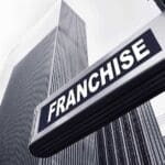 This image prominently features a sleek, modern sign with the word "FRANCHISE" set against a backdrop of towering skyscrapers. The composition conveys a strong corporate or urban environment, symbolizing the growth and expansion of franchise businesses within major cities. The inclusion of the R3volution Brands logo suggests a focus on the evolution and future of franchising, highlighting the company's role in shaping this industry sector. The stark, professional tone of the image underscores the significant influence and modern approach of franchise businesses in today's economic landscape.