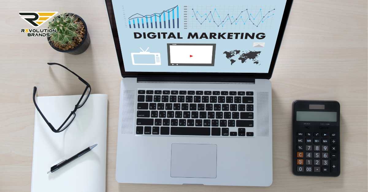 This image depicts a neatly organized workspace featuring a laptop displaying digital marketing analytics. The screen highlights graphs, a world map, and icons representing different media channels, emphasizing the global scope of digital marketing strategies. Accompanying the laptop are a notebook, a pen, glasses, a calculator, and a small potted cactus, creating a professional yet personal working environment. The R3volution Brands logo on the laptop ties this setting to the company, suggesting a focus on leveraging digital marketing tools for business growth and global reach.