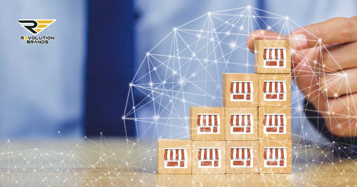 A conceptual image showing a hand arranging a pyramid of wooden blocks, each printed with a storefront symbol, set against a backdrop of digital network connections. The R3volution Brands logo in the top left corner enhances the theme of innovative, interconnected franchise development strategies. This image illustrates the concept of building and expanding a franchise network through strategic and technology-driven investments.