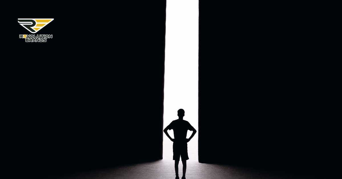 Silhouette of a confident individual standing with hands on hips, facing a large, bright vertical light opening within a dark room, symbolizing stepping into new opportunities. The stark contrast between the dark surroundings and the bright light represents the clarity and potential ahead. The R3volution Brands logo is discreetly positioned in the upper left corner, linking the image to corporate and entrepreneurial themes.